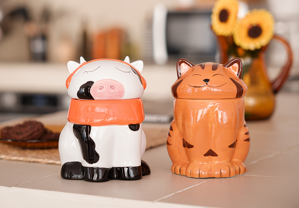 A cute ceramic mug shaped like a cow wearing an orange scarf and orange headphones. The cow has black and white spots and is sitting on a wooden surface. The mug has a whimsical and cozy design, perfect for fans of Lofi music and ChilledCow.