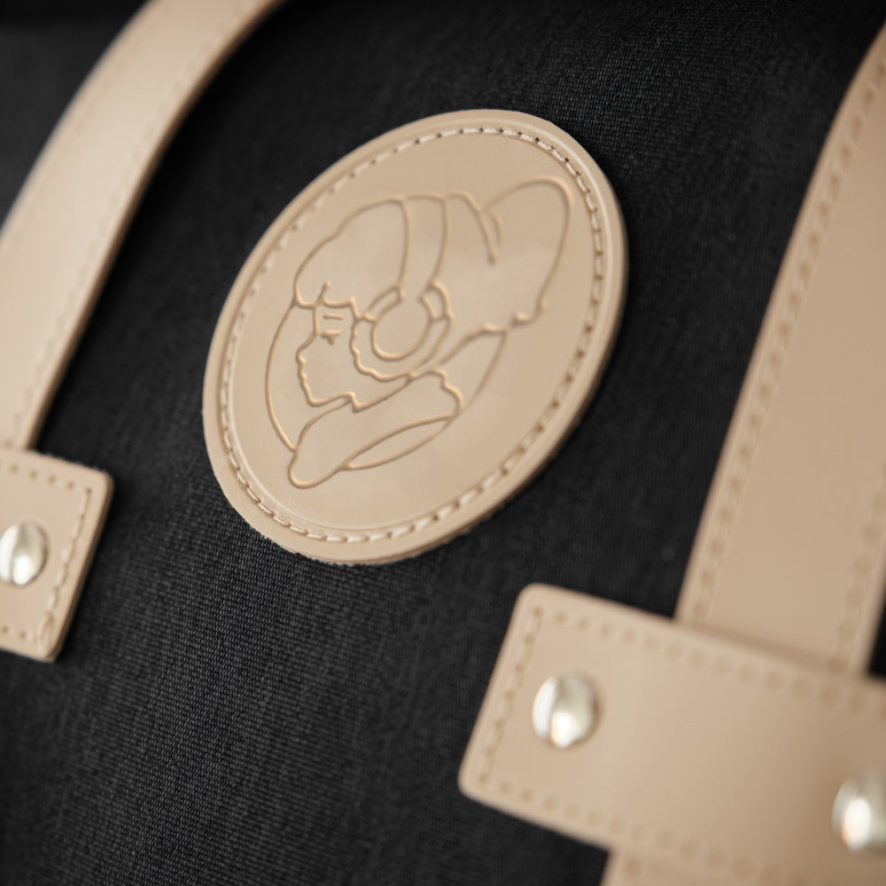 
                  
                    Close-up of the tan leather patch on a black Lofi Girl backpack, featuring an embossed design of the Lofi Girl wearing headphones. The detailed stitching and rivet accents highlight the high-quality craftsmanship and stylish details of the backpack.
                  
                