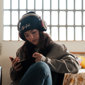 
                  
                    Person wearing a black beanie with the handwritten 'Lofi Girl' logo, headphones, and a grey sweatshirt, sitting comfortably while writing in a notebook. The room is softly lit with a grid-patterned window in the background, creating a focused and creative atmosphere.
                  
                