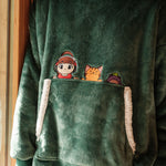 Close-up of a green Lofi Girl plaid hoodie showcasing a pocket with cute embroidered characters: Lofi Girl wearing headphones, a smiling orange cat, and a purple frog. The hoodie fabric is plush and cozy, with white sherpa lining on the pocket edges.