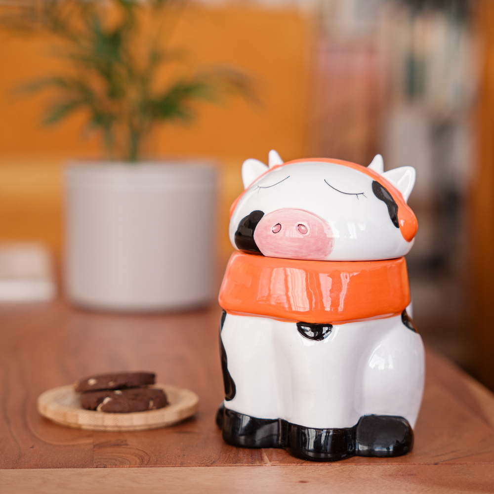 
                  
                    A cute ceramic mug shaped like a cow wearing an orange scarf and orange headphones. The cow has black and white spots and is sitting on a wooden surface. The mug has a whimsical and cozy design, perfect for fans of Lofi music and ChilledCow.
                  
                