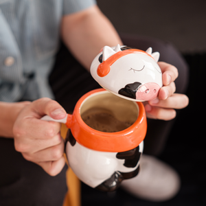 
                  
                    A cute ceramic mug shaped like a cow wearing an orange scarf and orange headphones. The cow has black and white spots and is sitting on a wooden surface. The mug has a whimsical and cozy design, perfect for fans of Lofi music and ChilledCow.
                  
                