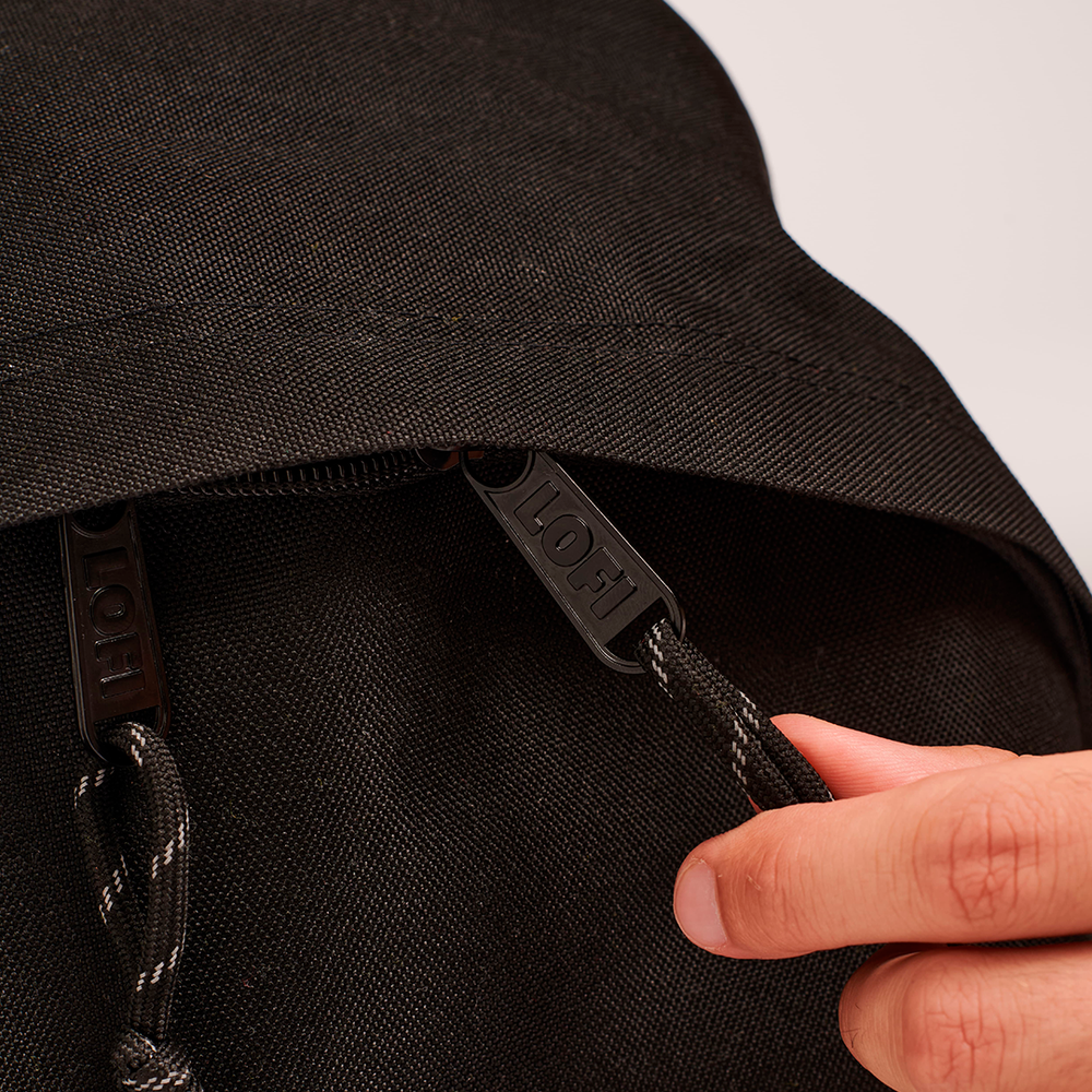 
                  
                    A close-up of the black Lofi Boy backpack's zipper pulls, embossed with the word "Lofi," with a hand holding one of the pulls.
                  
                