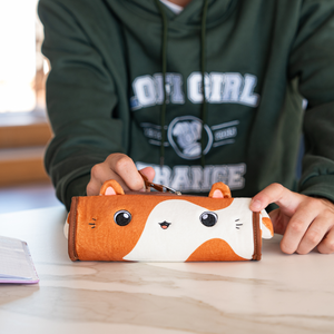 
                  
                    A close-up of a Lofi Cat pencil case held by someone wearing a green "Lofi Girl" hoodie. The pencil case is shaped like a cute cat face with big eyes and whiskers, designed in soft fabric in orange and white tones. The case looks plush and inviting, perfect for storing stationery or small items.
                  
                