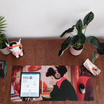 Overhead view of a desk setup featuring a "Lofi Girl" desk pad. The desk includes a plant in a pink pot, a "ChilledCow" plush toy, a tablet displaying a monthly planner, and a pencil case with headphones design on the right side. The desk pad shows the "Lofi Girl" character wearing headphones and writing in a notebook.