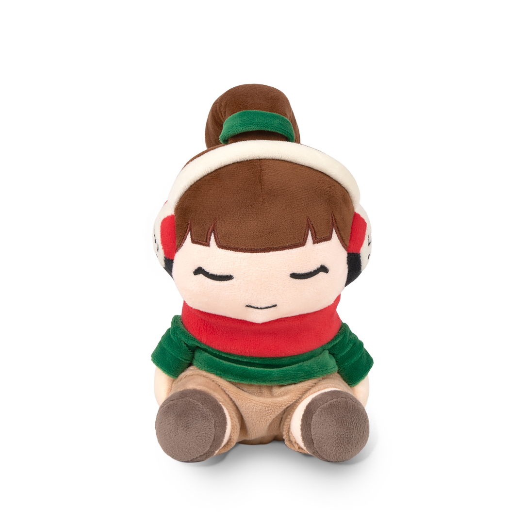 Plush toy of a girl with brown hair, wearing a green headband, red scarf, and brown shoes on a white background.