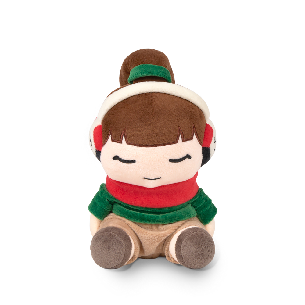 Plush toy of a girl with brown hair, wearing a green headband, red scarf, and brown shoes on a white background.