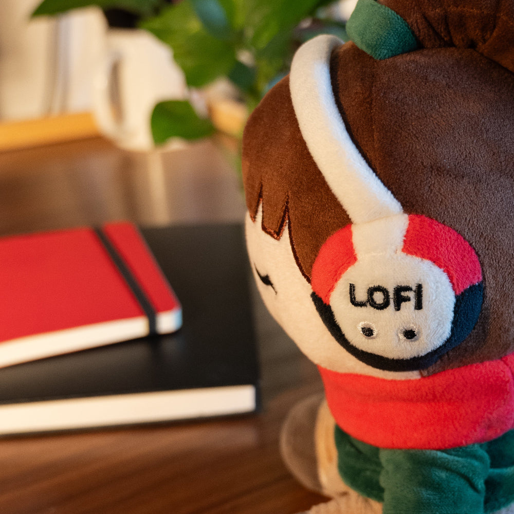 
                  
                    Plush toy with 'LOFI' headphones on a blurred background of books and plants
                  
                