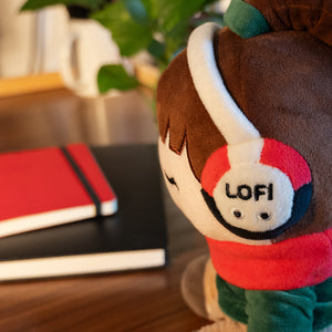 
                  
                    Plush toy with 'LOFI' headphones on a blurred background of books and plants
                  
                