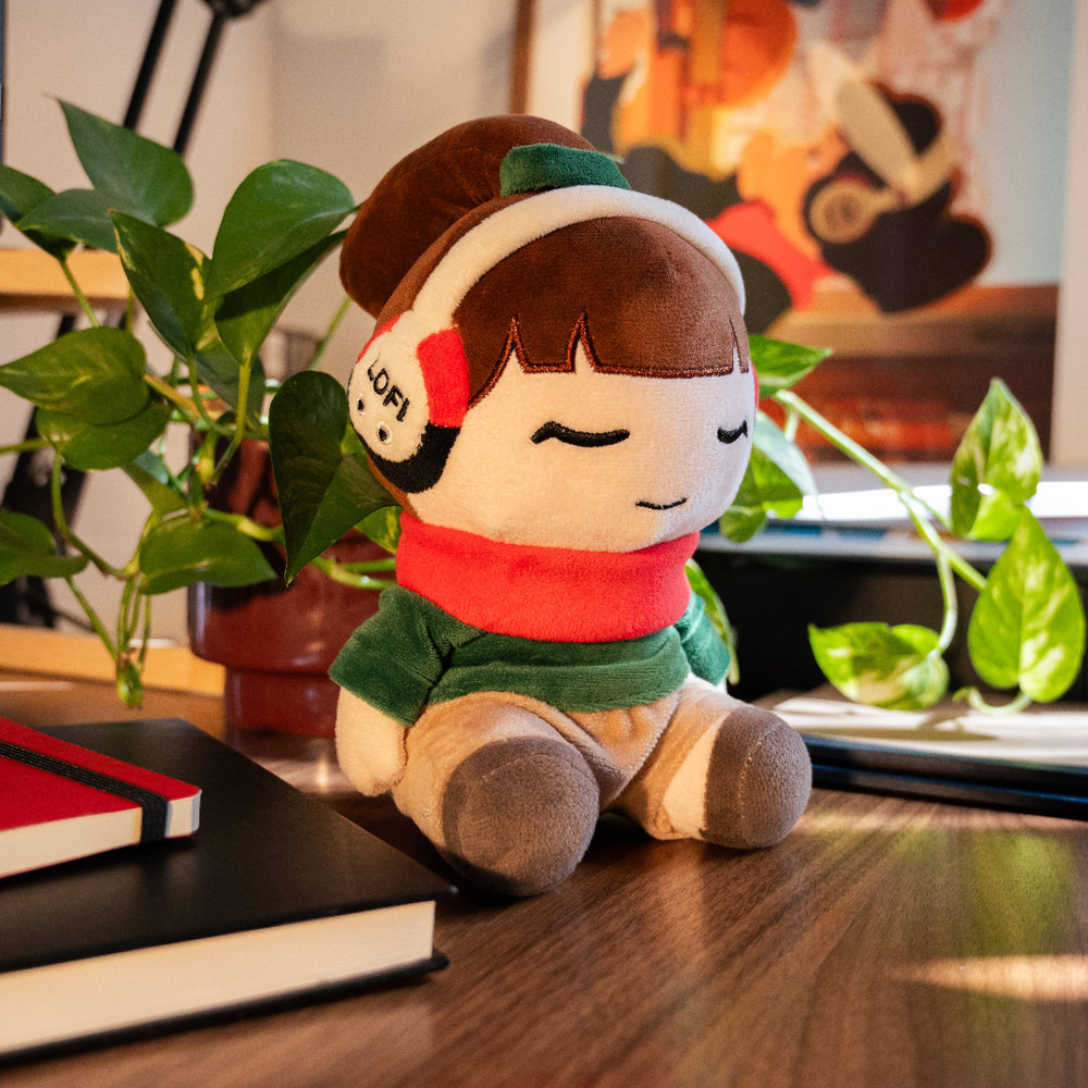 
                  
                    Plush toy with headphones on a desk with books and plants
                  
                