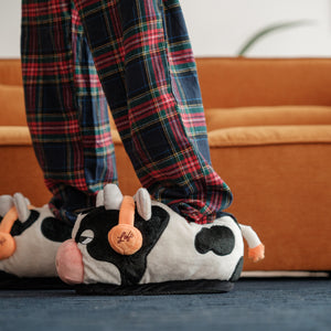 
                  
                    A close-up of Lofi Girl slippers shaped like cows with headphones, worn with plaid pajama pants. The focus is on the unique design and the comfort of the slippers against a soft blue carpet.
                  
                