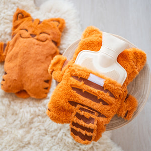 
                  
                    The back view of the orange plush hot water bottle cover, revealing the hot water bottle inside. The cover has a Velcro opening to easily insert or remove the bottle. The setting includes a wooden stool and a soft, fluffy rug in the background.
                  
                