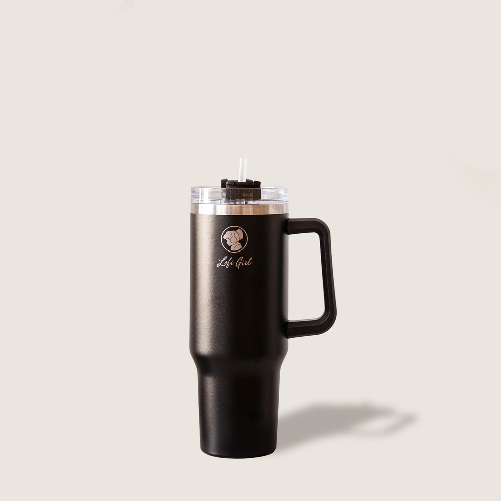 A black travel tumbler with the Lofi Girl logo on it. The tumbler is standing upright on a light beige background, showcasing its sleek design, handle, and transparent lid with a straw.