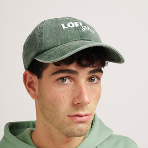 
                  
                    A portrait of a person wearing a vintage green cap with the "Lofi girl" logo embroidered in white on the front. The person is looking slightly to the side, and the cap has a faded, vintage style that complements the casual outfit.
                  
                