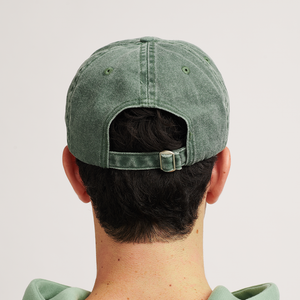 
                  
                    A close-up rear view of a person wearing a vintage green cap. The cap features an adjustable strap and buckle at the back, offering a customized fit. The cap has a slightly faded, worn look, adding to its vintage style.
                  
                