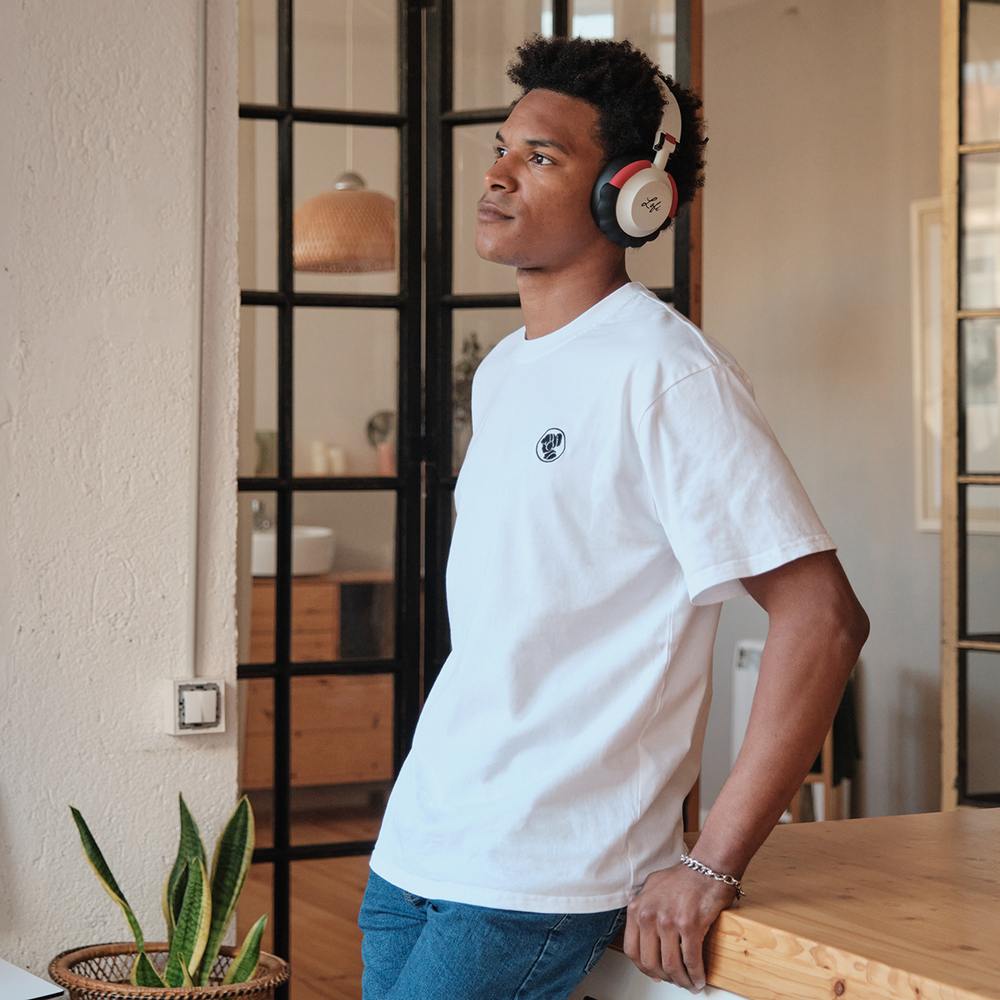 
                  
                    Person wearing a white Lofi Girl t-shirt with a small, round logo on the chest, paired with jeans and headphones. They are leaning casually against a wooden counter in a stylish, well-lit room with modern decor, conveying a relaxed and thoughtful mood.
                  
                