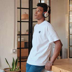 
                  
                    Person wearing a white Lofi Girl t-shirt with a small, round logo on the chest, paired with jeans and headphones. They are leaning casually against a wooden counter in a stylish, well-lit room with modern decor, conveying a relaxed and thoughtful mood.
                  
                