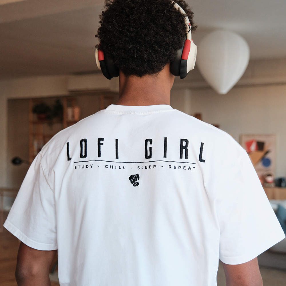 
                  
                    Back view of a person wearing a white Lofi Girl t-shirt with the bold black text 'Lofi Girl' across the back, accompanied by the tagline 'Study • Chill • Sleep • Repeat' and a small fist icon. They are wearing headphones and standing in a modern, tastefully decorated room, conveying a laid-back and focused vibe.
                  
                