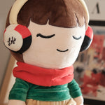 A close-up shot of the Lofi Girl plush, highlighting its serene expression with closed eyes and a gentle smile. The plush's soft texture and intricate details, like the "Lofi" branding on the earmuffs, showcase its high-quality craftsmanship and unique character design.