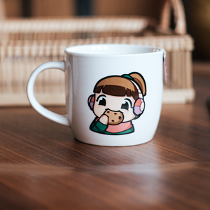 
                  
                    A white ceramic mug featuring the Lofi Girl in headphones, holding a cookie close to her mouth, with a playful expression. The mug is placed on a wooden surface.
                  
                